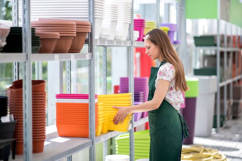 Woman employee picking up several yellow plastic bins off of a shelf.